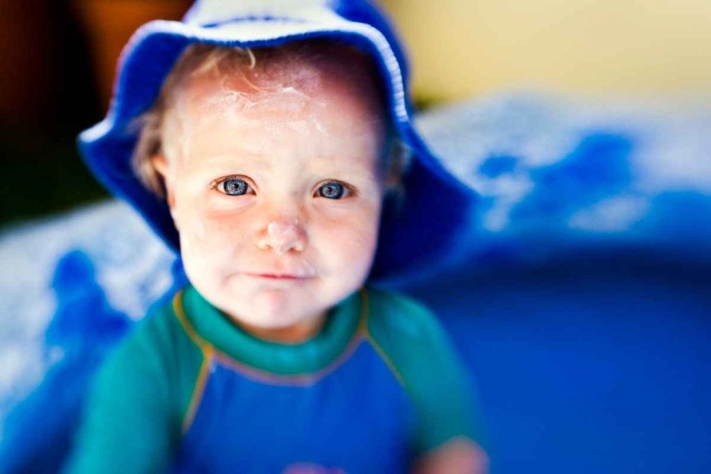 Bebê se protegendo do sol com chapéu e protetor solar